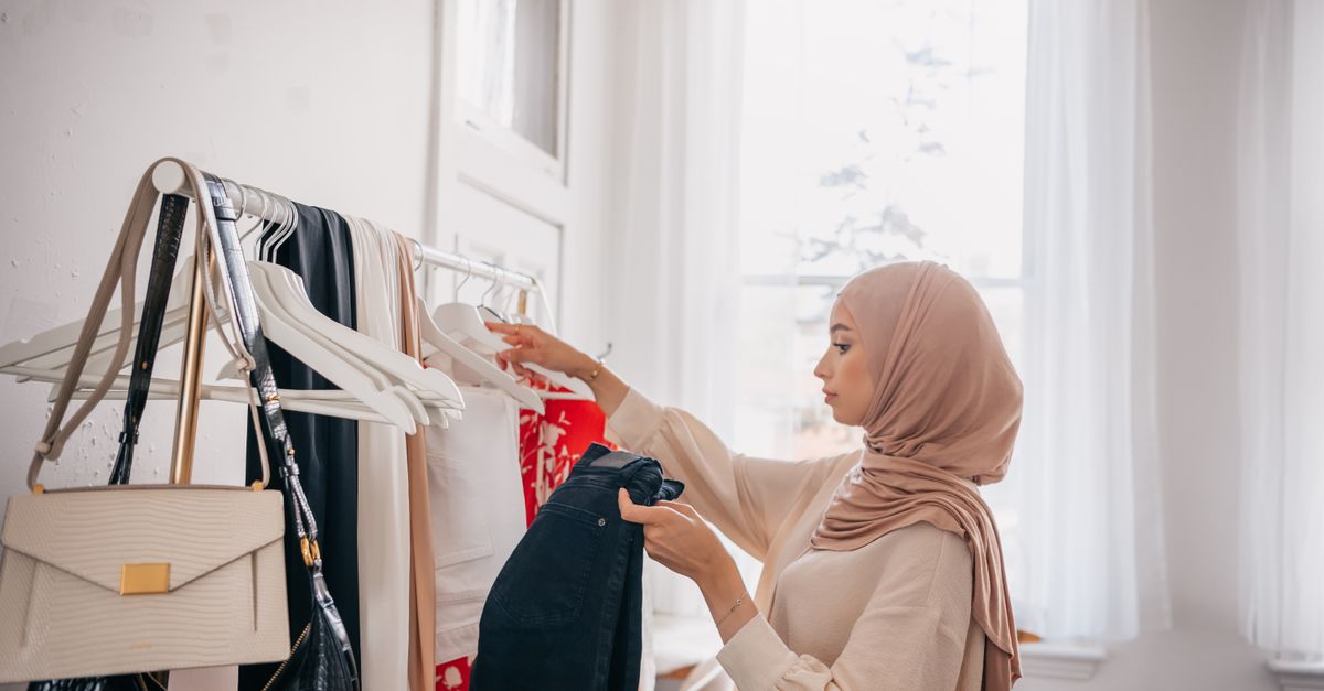 Young woman in hijab browsing clothes on rack indoors. Fashionable and modern.